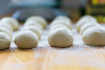 A close-up of small, white balls of home-made dough for a multi-layered banitsa and pizza on a kitchen table, flour for kneading. Shallow depth of focus.