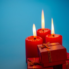Three burning red candles and Christmas boxes on a blue background.