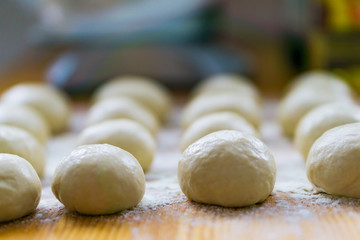 A close-up of small, white balls of home-made dough for a multi-layered banitsa and pizza on a kitchen table, flour for kneading. Shallow depth of focus.