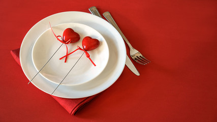 Romantic table setting for Valentines day. Valentines day table setting with two hearts, fork and knife tablecloth on red background. Valentine's day background. Red space for your text