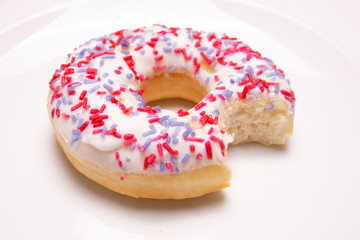 closeup of a donut on a white plate with a bite taken out on a white background