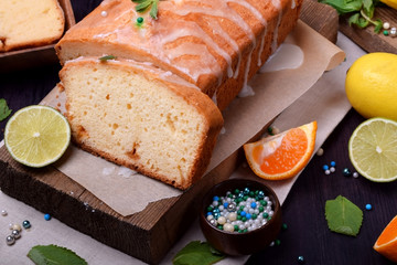 Citrus sponge cake and a piece of it on the board surrounded by the fruits