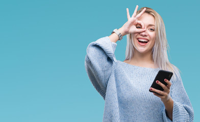 Young blonde woman texting sending message using smartphone over isolated background with happy face smiling doing ok sign with hand on eye looking through fingers