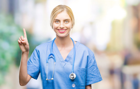 Young beautiful blonde doctor surgeon nurse woman over isolated background showing and pointing up with finger number one while smiling confident and happy.