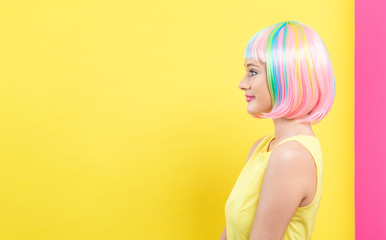 Beautiful woman in a bright colorful wig on a split yellow and pink background