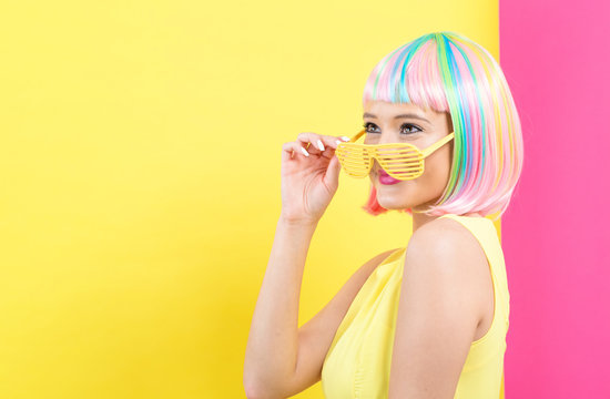Young woman in a colorful wig with shutter shades sunglasses on a split yellow and pink background