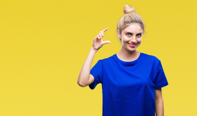 Young beautiful blonde and blue eyes woman wearing blue t-shirt over isolated background smiling and confident gesturing with hand doing size sign with fingers while looking and the camera
