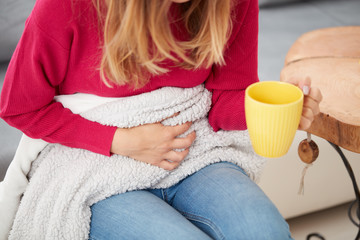 Sick girl holding cup and drinking coffee / tea on a couch.