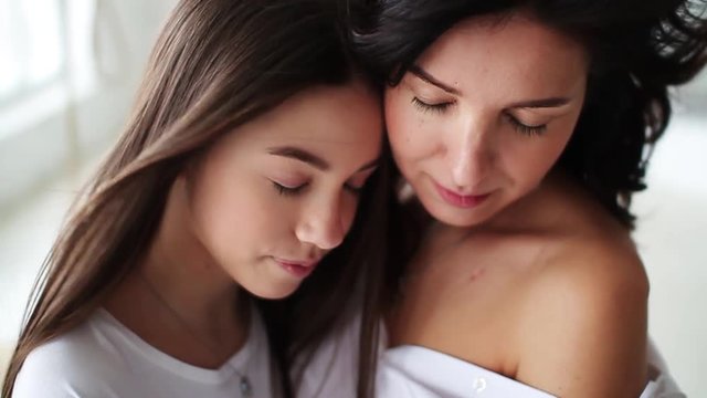 Beautiful closed eyes mom and daughter hugging showing love and affection in white studio smile happy family mother together cute pretty teenager portrait close up slow motion