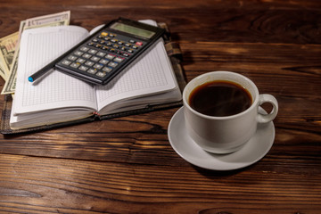 Cup of coffee and notepad with dollars, pencil and calculator on wooden desk. Financial concept