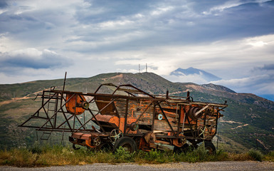 Fototapeta premium rusting and decaying combine harvester abandoned on mountain roadside with dramatic mountains behind.