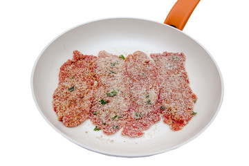 Slices of breaded raw meat in a pan on a white background