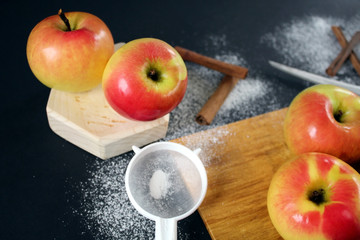 Pink lady apples on wood board at black background. Apple for baking. On table lie ripe apples, knife and cinnamon. Cooking baking roses step by step. Step one to prepare the apples before cutting