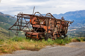 Fototapeta premium rusting and decaying combine harvester abandoned on mountain roadside with dramatic mountains behind.