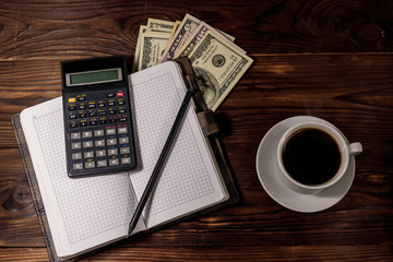 Cup of coffee and notepad with dollars, pencil and calculator on wooden desk. Top view. Financial concept