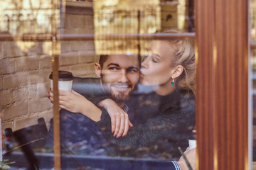 Beautiful girl sitting on her boyfriend's lap on the cafe behind the window.