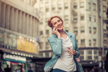 Fototapeta premium Confident mid-age woman talking on a cell phone in the street