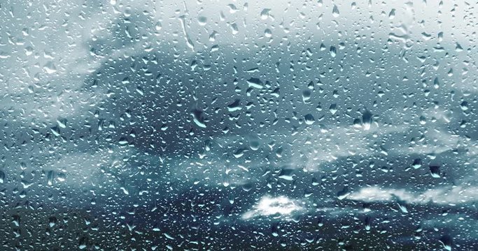 Water drops on a window at a rainy day with clouds time lapse background. Selective focus used. 