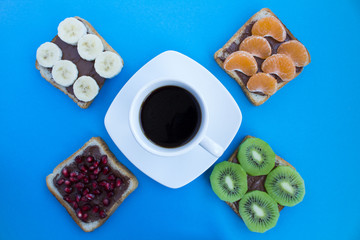 Obraz na płótnie Canvas Black coffee in the white cup and sandwiches with chocolate cream and fruit on the blue background.Top view.