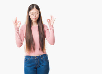 Young Chinese woman over isolated background wearing glasses relax and smiling with eyes closed doing meditation gesture with fingers. Yoga concept.