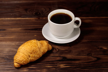 Cup of coffee and fresh croissant on wooden table