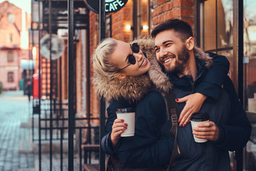 A beautiful girl hugs her boyfriend near the cafe outside.