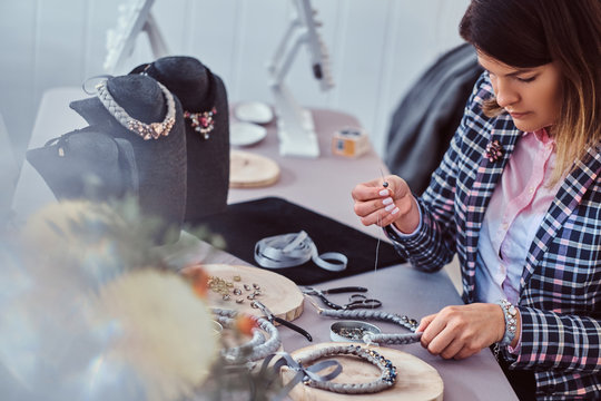 Elegantly dressed woman makes handmade necklaces, working with needles and thread in workshop.