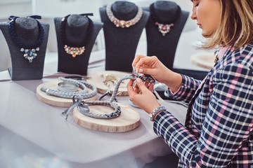 Elegantly dressed woman makes handmade necklaces, working with needles and thread in workshop.