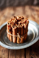 Bunch of Cinnamon sticks on a metallic rustic plate over a wooden table.