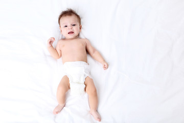 Cute baby in diaper lying on white bed