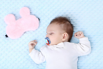 Cute baby sleeping in bed near pink mask