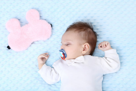 Cute baby sleeping in bed near pink mask