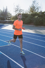 Fototapeta na wymiar Athlete running on a running track alone. Runner sprinting on a blue rubberized running track.