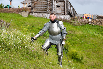 A knight in armor tears daisy flowers. Knightly armor and weapon. Semi - antique photo.