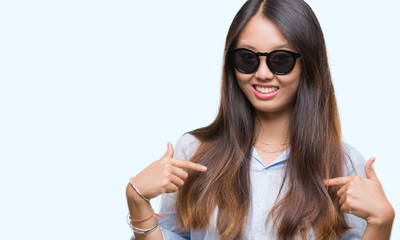 Young asian woman wearing sunglasses over isolated background looking confident with smile on face, pointing oneself with fingers proud and happy.