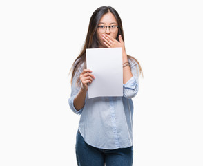 Young asian woman holding blank paper over isolated background cover mouth with hand shocked with shame for mistake, expression of fear, scared in silence, secret concept