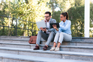 Obraz premium Young businessman and businesswoman using laptop and tablet, sitting outside in a park having a business meeting together as a team.