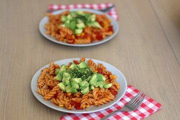 Two plates of pasta with tomato sauce, peppers, corn, avocado and herbs. Selective focus.