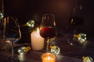 Holidays composition made of glass of red wine, candles and garlands on a dark background