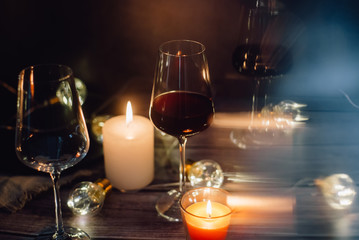 Holidays composition made of glass of red wine, candles and garlands on a dark background