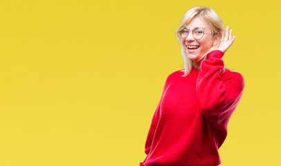 Young beautiful blonde woman wearing sweater and glasses over isolated background smiling with hand over ear listening an hearing to rumor or gossip. Deafness concept.