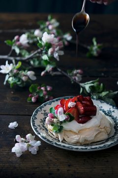 Crema di Balsamico being drizzled onto a strawberry pavlova decorated with fruit blossoms