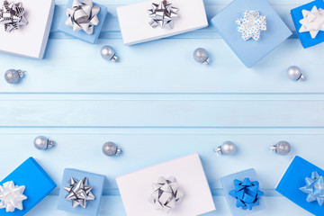 Along the edges of the light blue background, blue and white gift boxes and Christmas silver balls are laid out. Empty place for text and inscriptions, copy space.