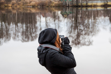 Fototapeta na wymiar girl taking pictures on camera during a trip to the lake cold late autumn reflection of trees, sky, forest