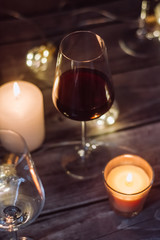 Holidays composition made of glass of red wine, candles and garlands on a dark background