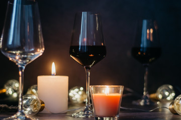 Holidays composition made of glass of red wine, candles and garlands on a dark background