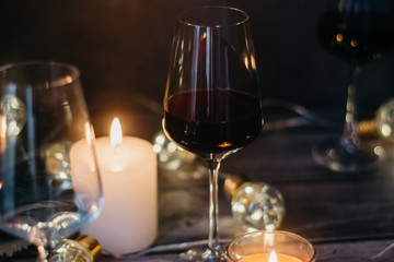 Holidays composition made of glass of red wine, candles and garlands on a dark background