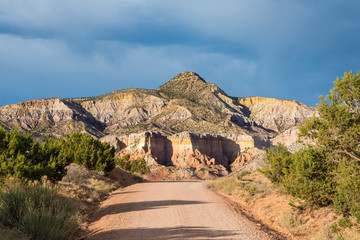 Dirt road leading to a colorful desert mountain, cliffs, and rock formations  under a stormy sky in Ghost Ranch near Abiquiu, New Mexico