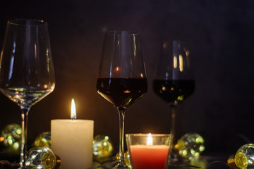 Holidays composition made of glass of red wine, candles and garlands on a dark background