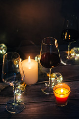 Holidays composition made of glass of red wine, candles and garlands on a dark background